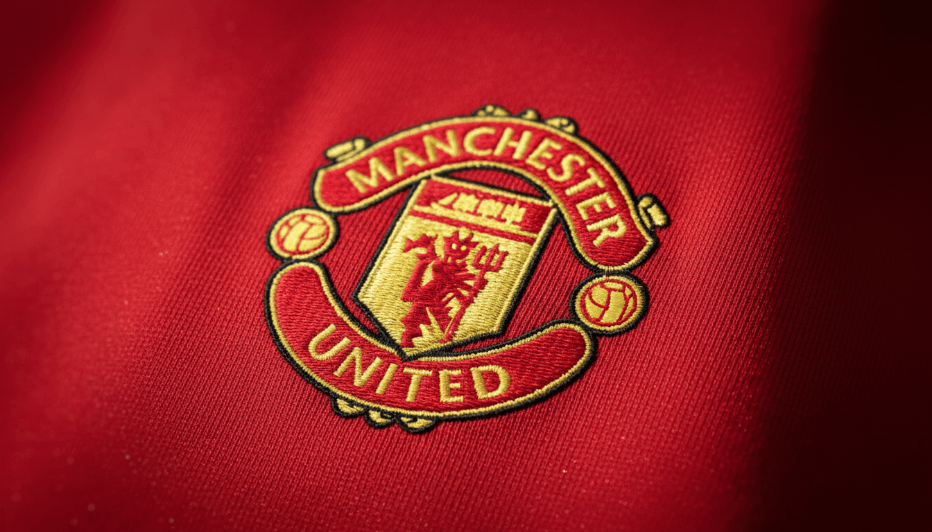 Close-up detail of a Manchester United club badge embroidered on a red fabric, symbolizing the club's identity and the potential arrival of Aurelien Tchouameni.
